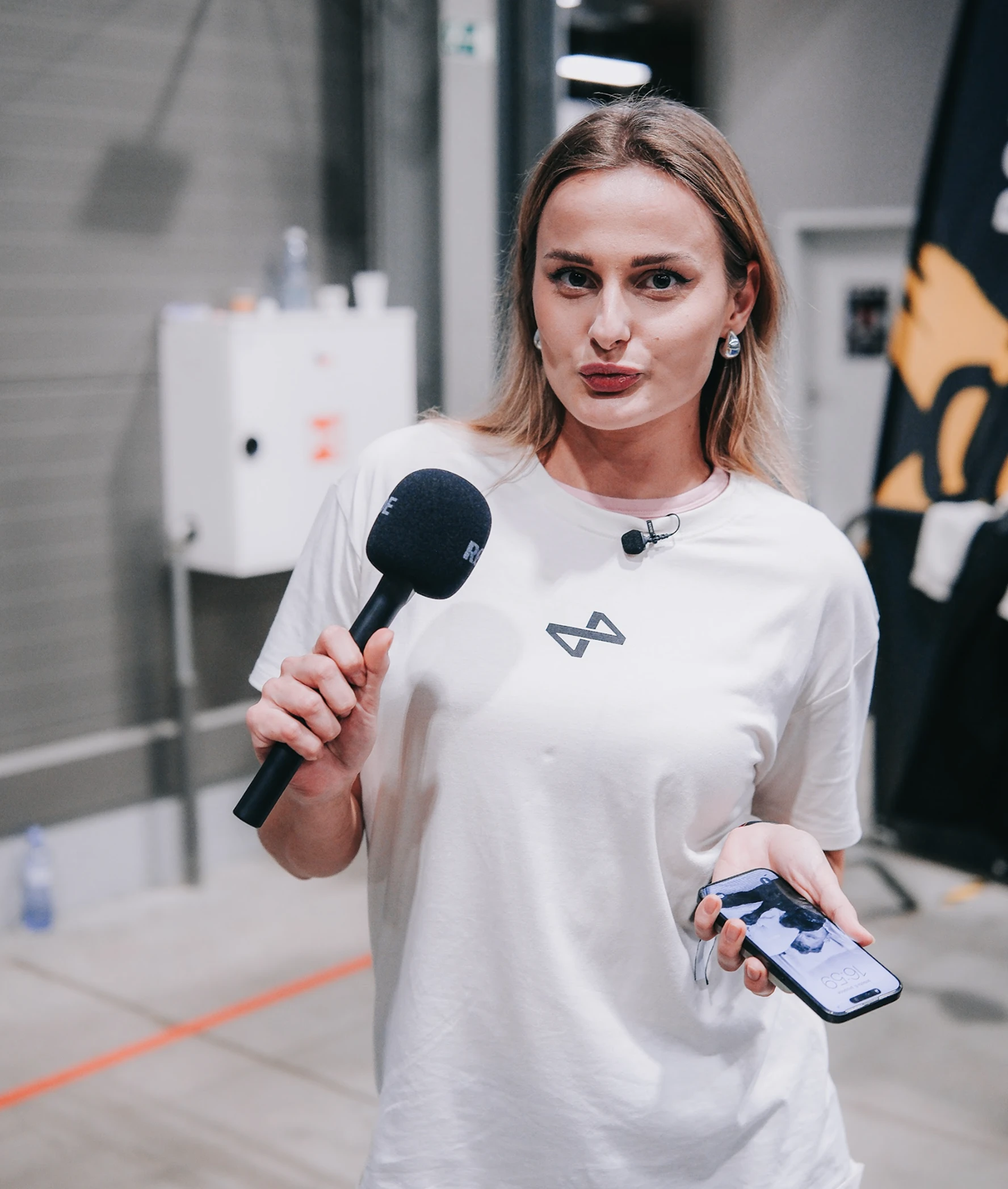 Bcross Run brand ambassador holding microphone and iPhone, wearing white T-shirt with BCR logo at race expo
