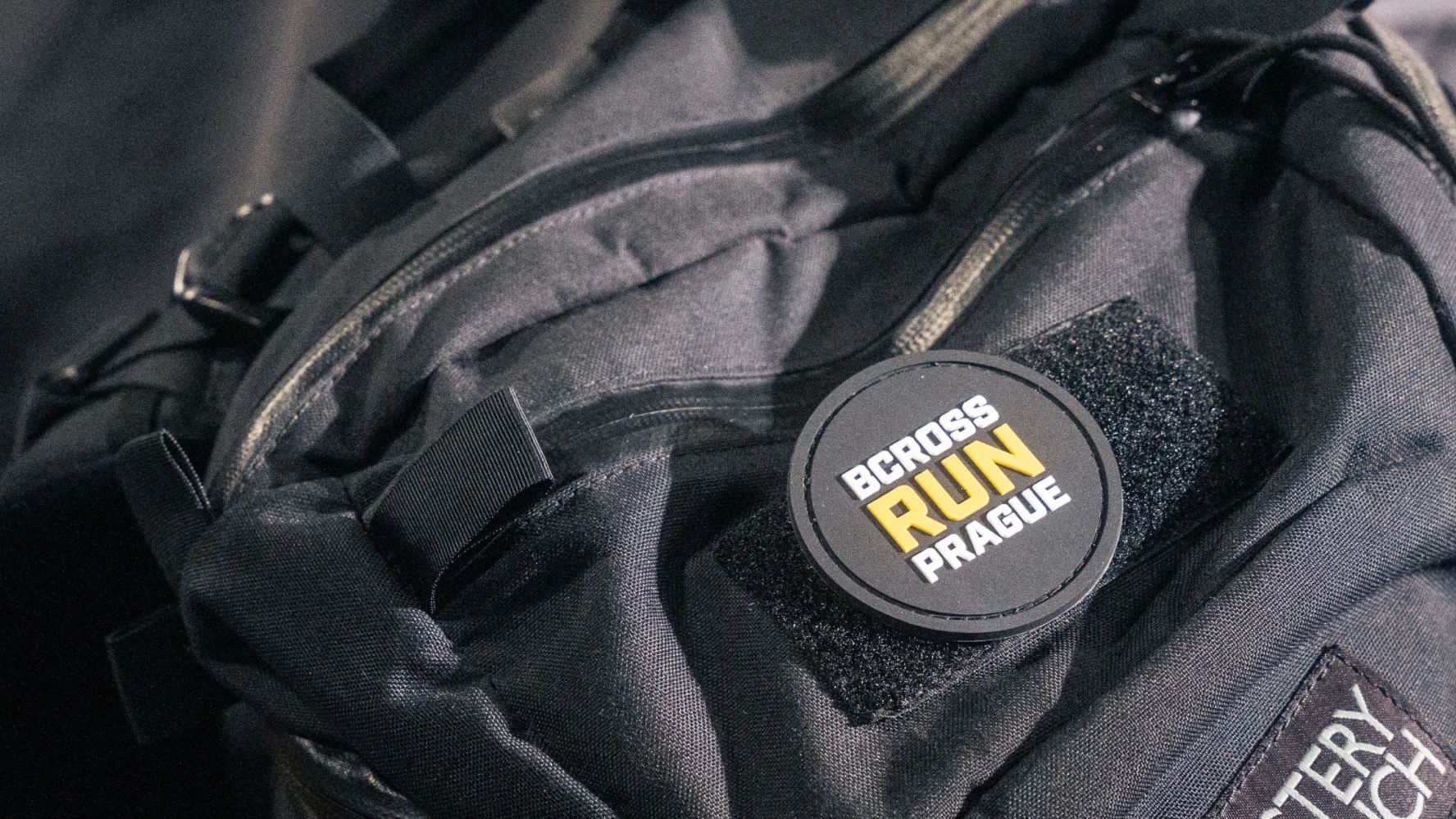 Bcross Run woven round badge reading BCROSSRUN PRAGUE on a black tactical backpack