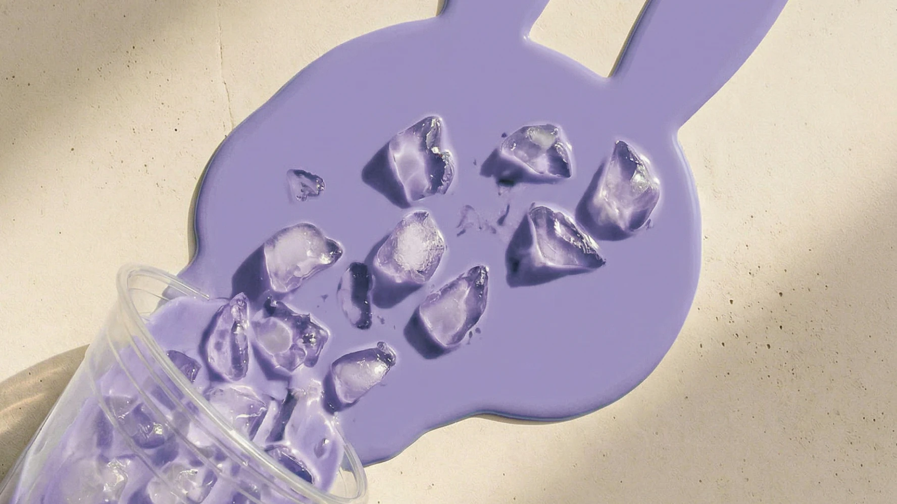 Boba tea image 1 — clear cup tipping purple ice cubes onto giant bunny-cup silhouette splash on beige backdrop